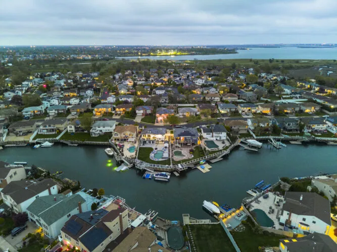 Small illuminated town on sea channel bank with boats and yachts on piers against cloudy sky, twilight in Nassau County, New York